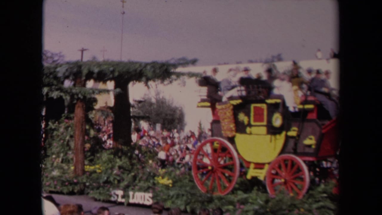 1967 Los Angeles parade frame showing a yellow and black stagecoach float, passengers, red wheels, greenery, and spectators.