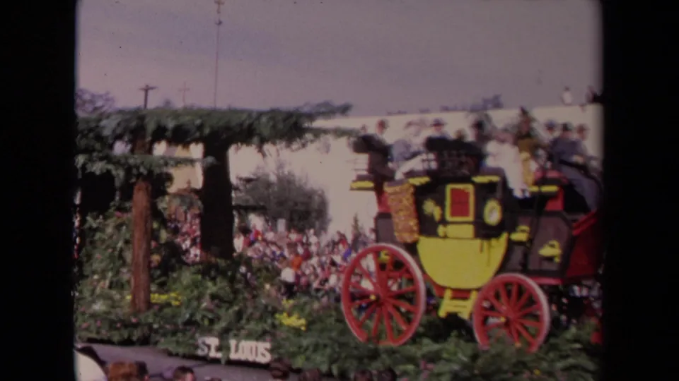 1967 Los Angeles parade frame showing a yellow and black stagecoach float, passengers, red wheels, greenery, and spectators.