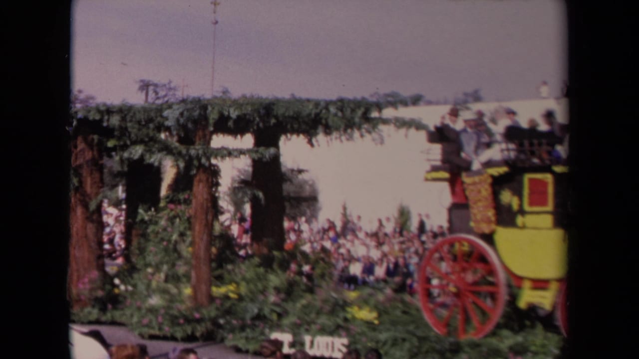 1967 Los Angeles parade view with a stagecoach float at right, floral arch structure, spectators, and partial route signage.