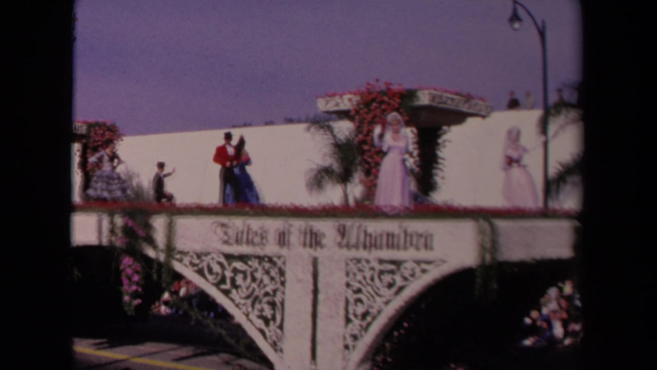 Tales of the Alhambra parade float in Los Angeles, 1967, with formally dressed performers and red flowers along the platform.