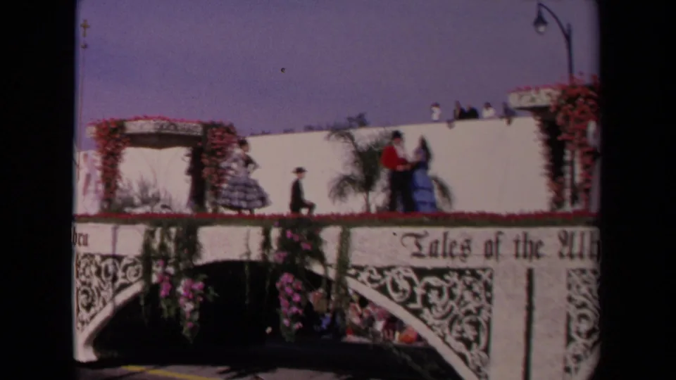 The Tales of the Alhambra float continues past the camera in 1967 Los Angeles, with costumed figures, flowers, and spectators below.