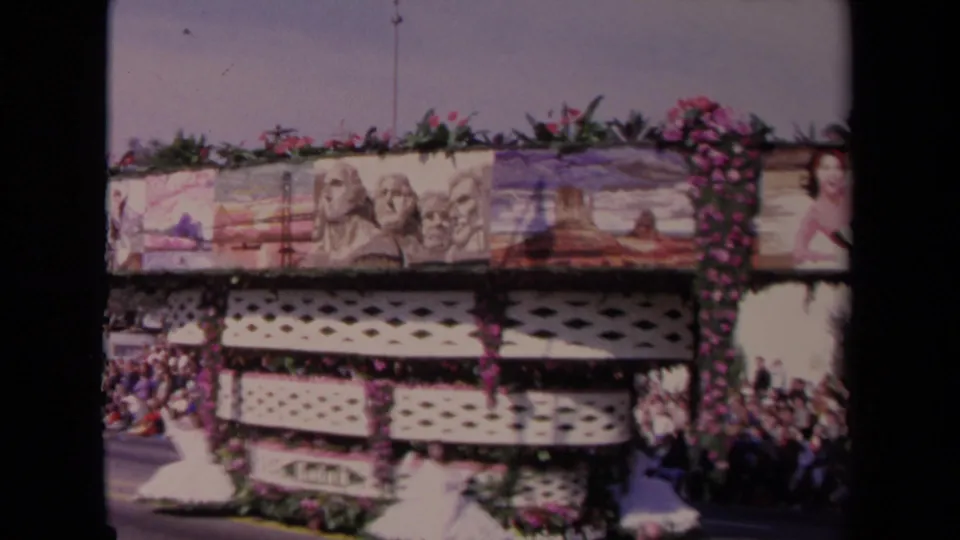 The decorated 1967 Los Angeles float shows scenic paintings, flowers, lattice panels, and a pageant figure in white near the curb.