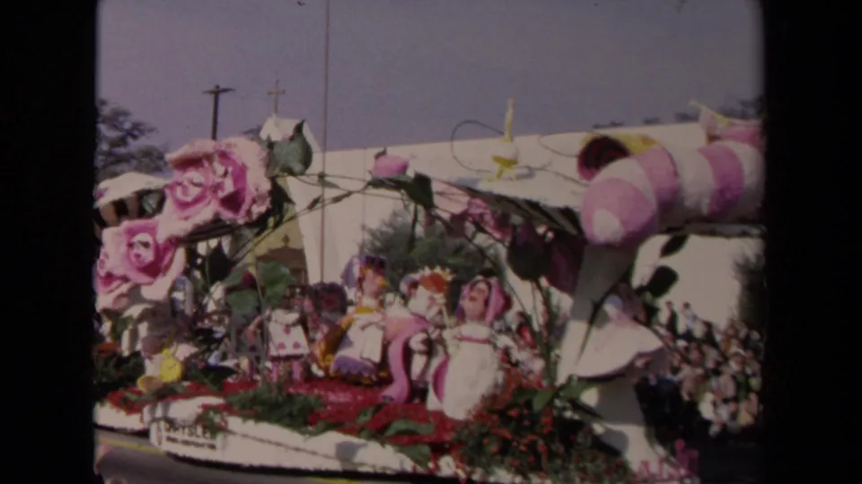 A closer 8mm view shows pink roses, fantasy-style figures, red floral trim, and spectators watching the float pass.
