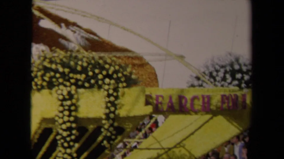 A yellow and purple Lions International float passes in 1967 Los Angeles, with floral decoration and part of a globe-shaped structure visible.