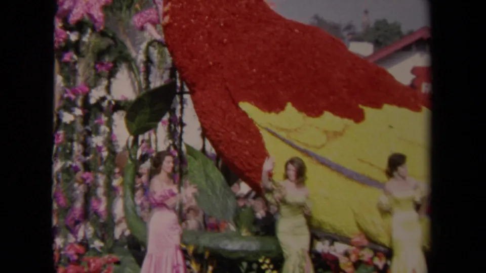 1967 Los Angeles 8mm frame showing a floral parrot float with women in gowns and spectators along the route.