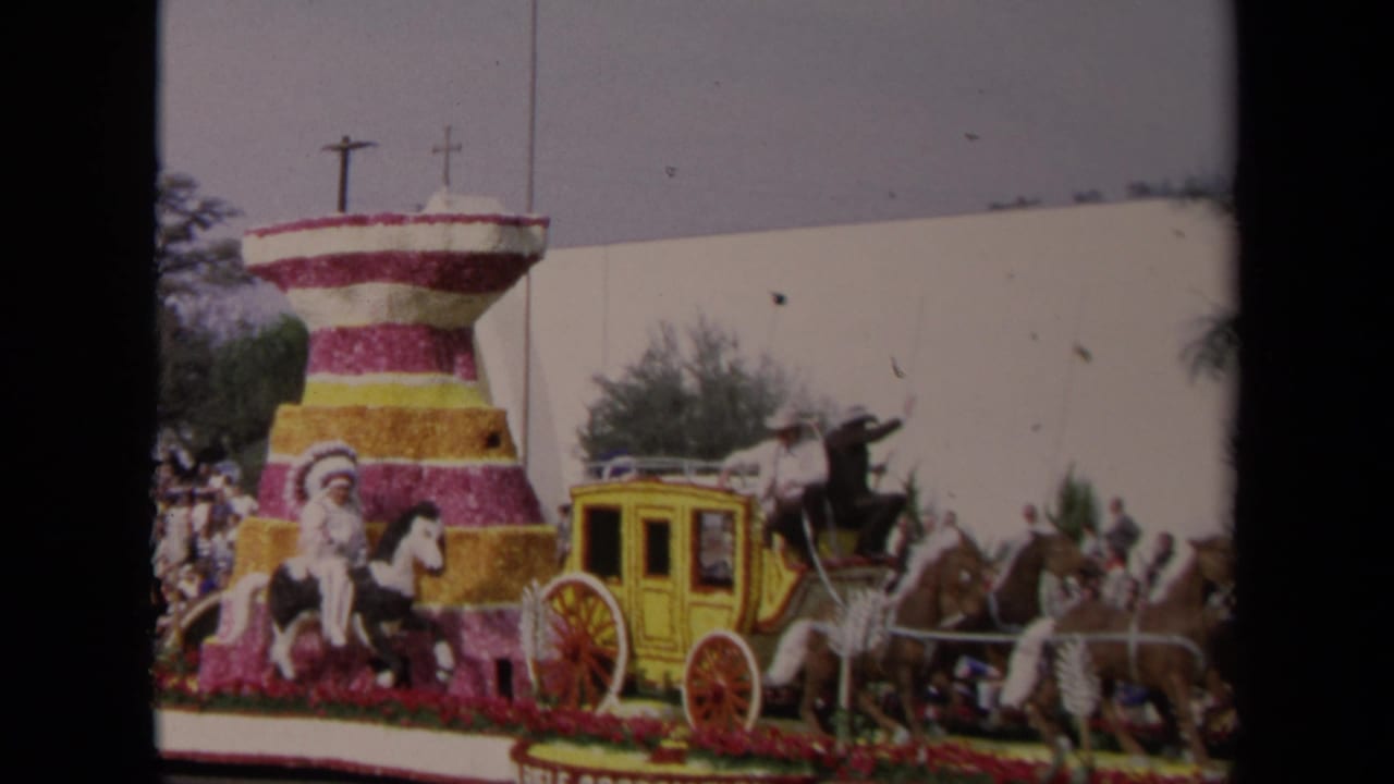 1967 Los Angeles parade float with a tiered floral structure, yellow stagecoach, horses, costumed riders, and crowds behind it.