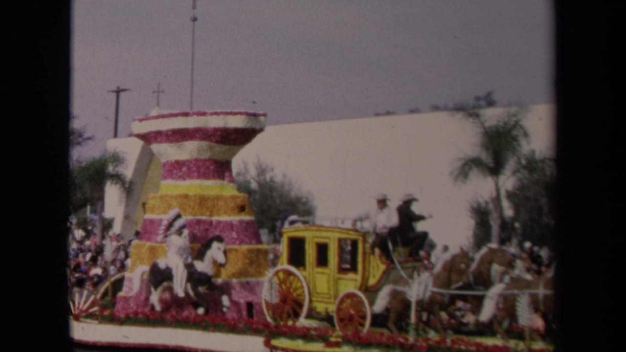 Parade float with yellow stagecoach, horses, costumed riders, and a crowd along the street.