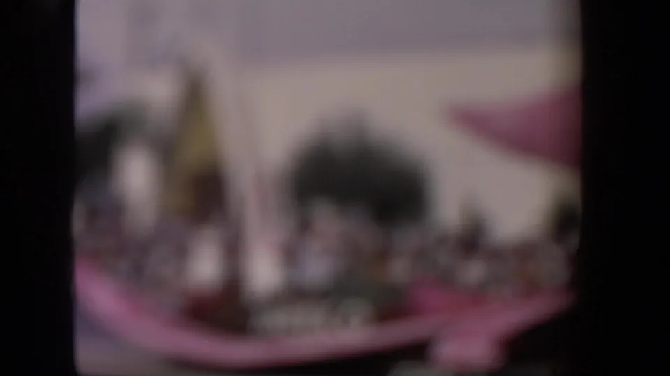 Soft-focus 1967 Los Angeles parade frame showing blurred spectators, float color, and the outline of the nearby building.