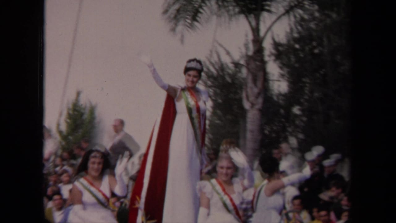 1967 Los Angeles parade frame showing a crowned queen in a white gown waving from a float with sash-wearing attendants nearby.