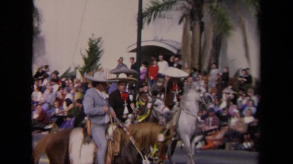 1967 Los Angeles parade view with horseback riders, including a man in a sombrero, passing spectators beneath palm trees.