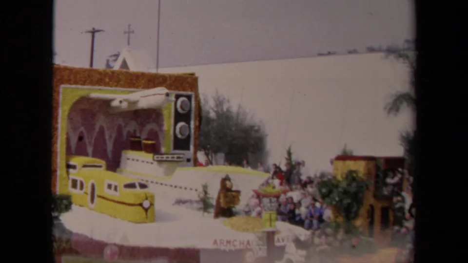 1967 Los Angeles 8mm frame showing a decorated parade float with a yellow train, submarine-like body, oversized television prop, and curbside spectators.