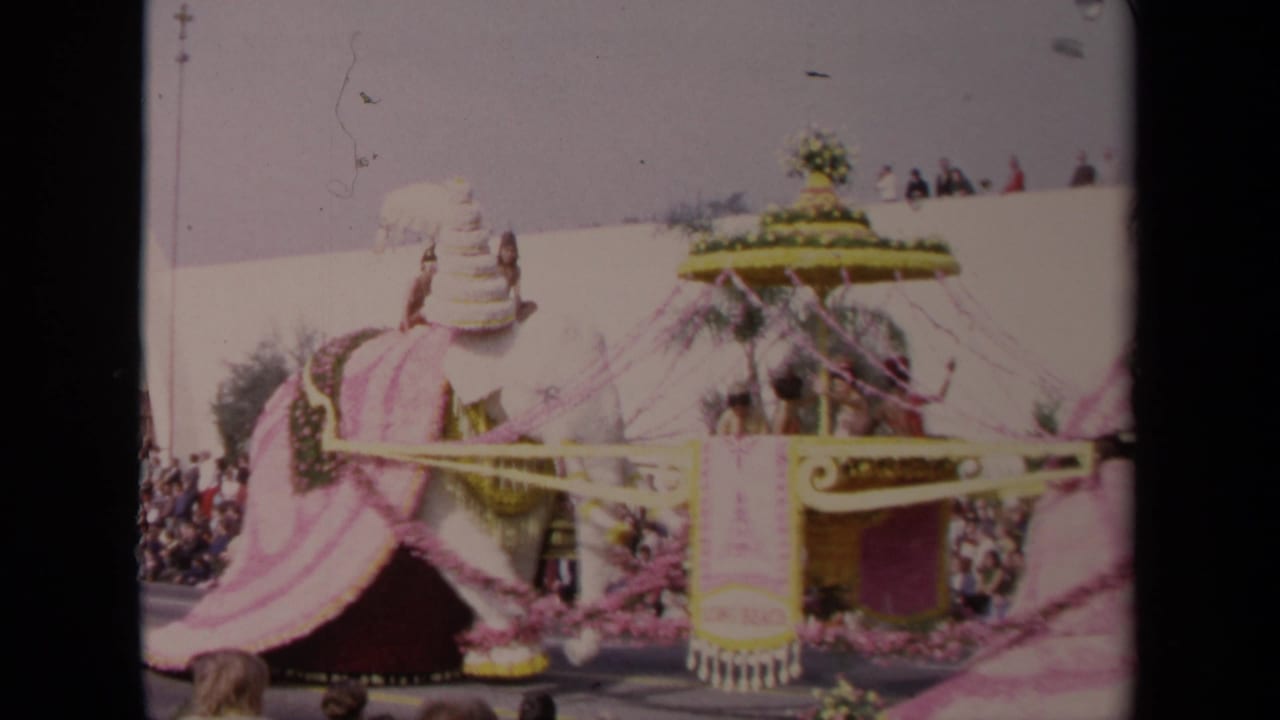 1967 Los Angeles 8mm frame showing a large decorated elephant float with pink fabric, floral trim, riders, and spectators watching from the curb.