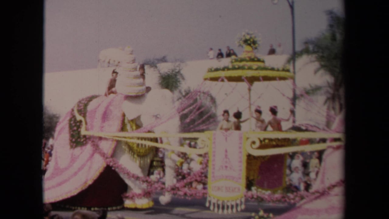Elephant float with yellow canopy, pink streamers, costumed riders, and spectators in the background.