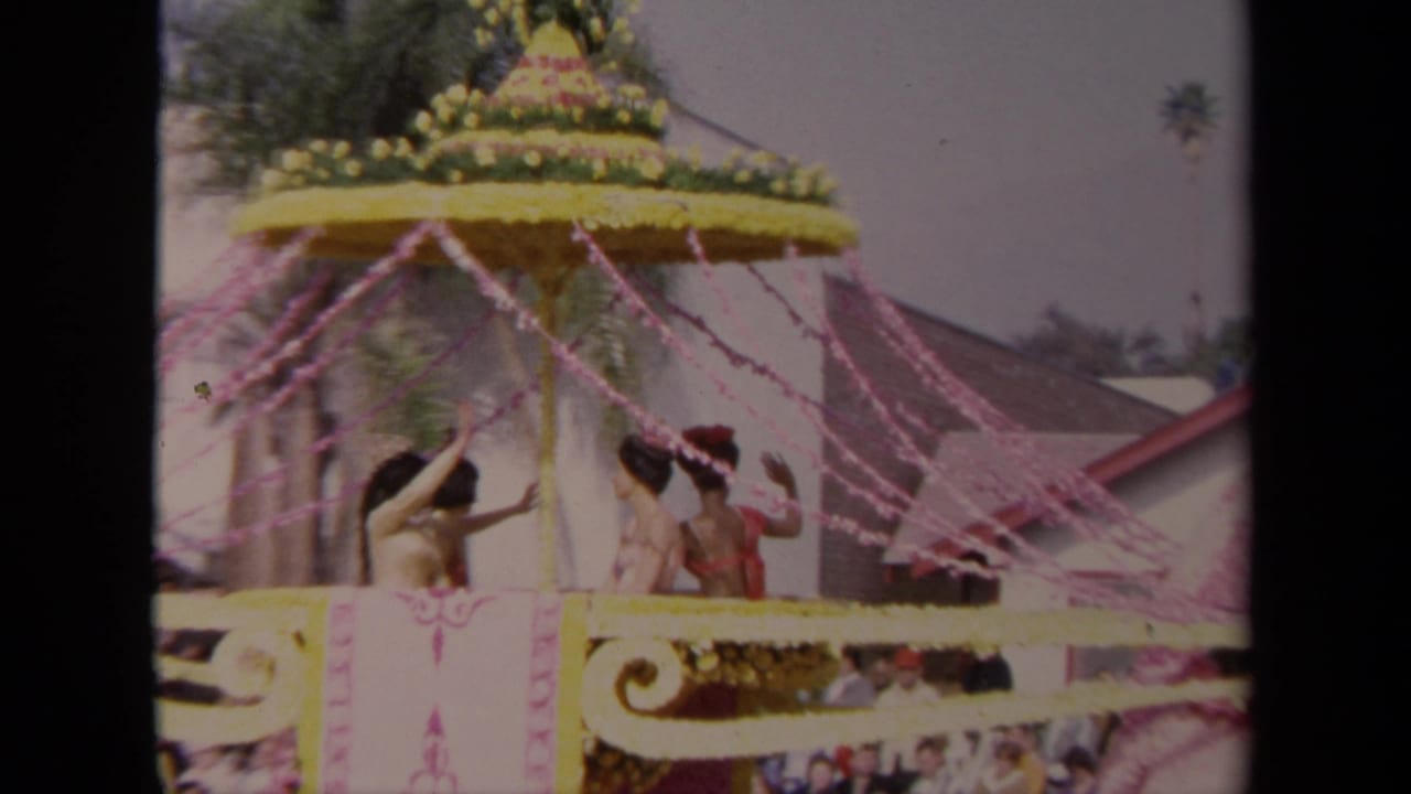 1967 Los Angeles parade frame focused on costumed riders beneath a yellow floral canopy, with pink streamers and spectators visible below.