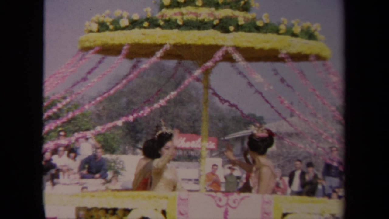 1967 Los Angeles home-movie frame of a decorated parade float with women waving below pink streamers and floral trim.
