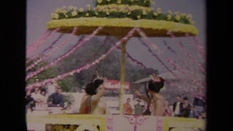 1967 Los Angeles home-movie frame of a decorated parade float with women waving below pink streamers and floral trim.