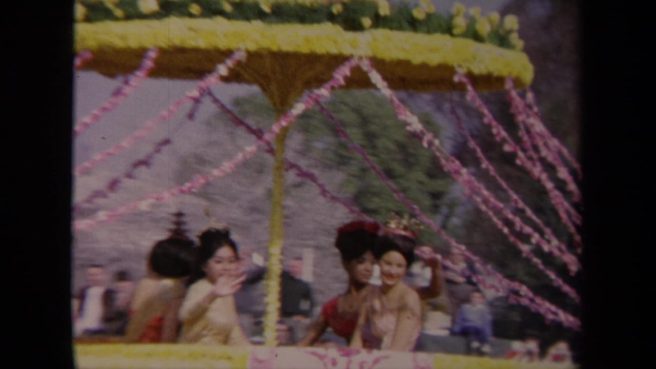 1967 Los Angeles parade frame showing women in formal attire smiling and waving from a decorated float.