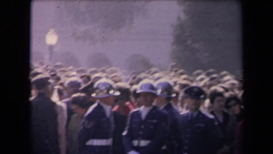 Soft 8mm frame of a dense outdoor crowd with uniformed guards visible in front, associated by metadata with the 1967 Reagan inauguration in Sacramento.