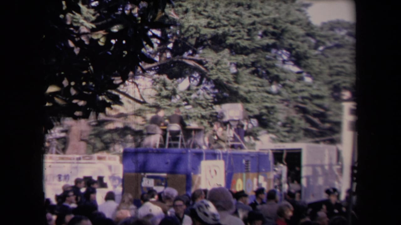Outdoor political crowd with a mobile news unit, camera operators, banners, and trees visible in 1967 Sacramento inauguration footage.