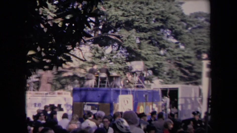 Outdoor political crowd with a mobile news unit, camera operators, banners, and trees visible in 1967 Sacramento inauguration footage.