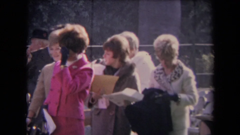 A group of formally dressed women at the outdoor 1967 Sacramento gathering hold papers and look toward activity off camera.