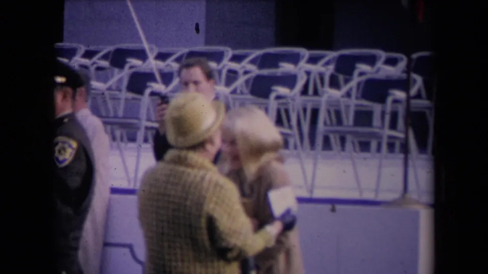 A uniformed attendee stands at the left edge while the woman in the yellow hat and the blonde woman remain close together.