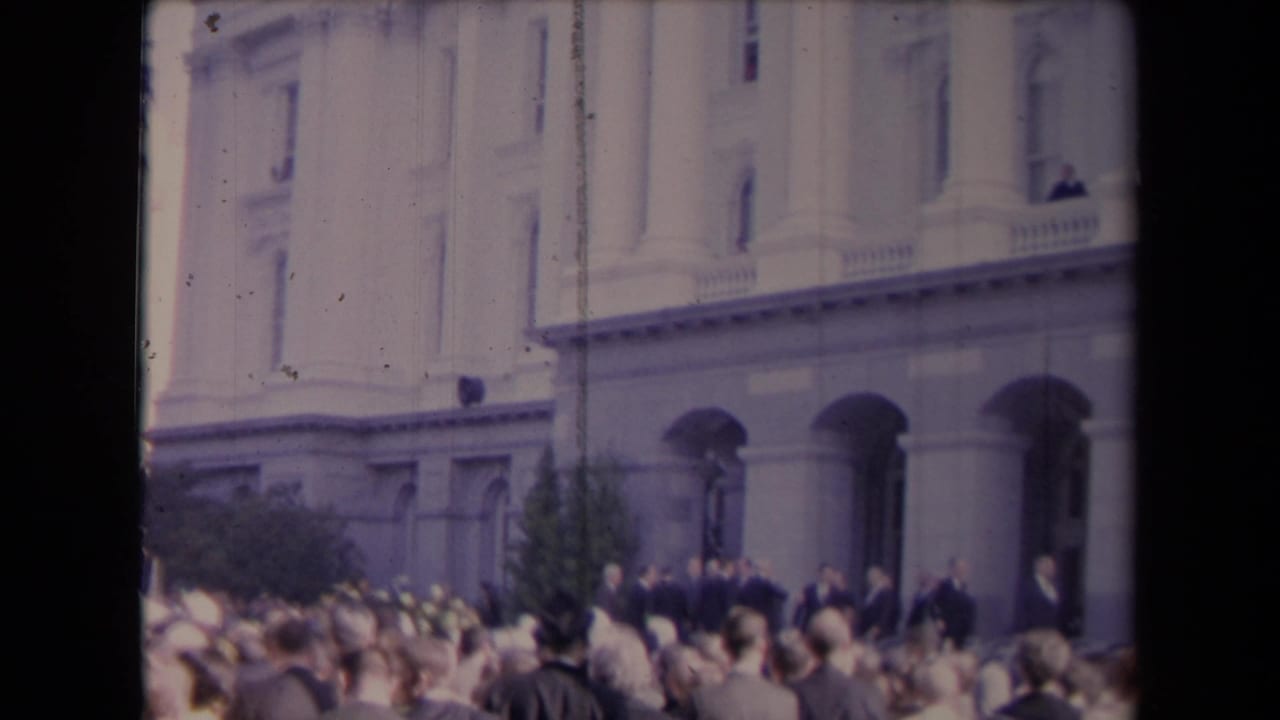 Crowd gathered outside a classical building with arched entrances and columns.