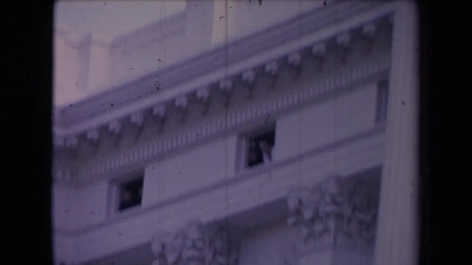 Soft 8mm view of a classical facade where a person appears at an upper window, with heavy grain and color shift.