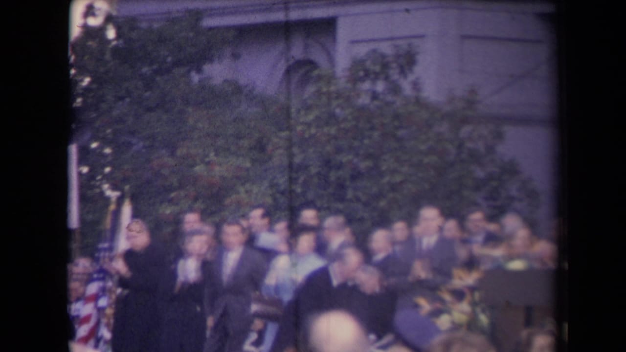 Crowd of formally dressed people gathered outdoors near a building facade.