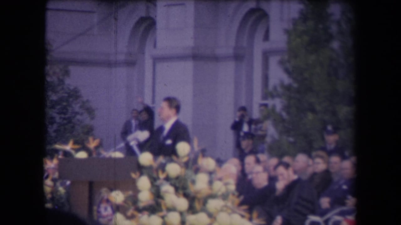 Ronald Reagan appears at a flower-lined outdoor podium during a reported 1967 Sacramento inauguration event, with spectators seated nearby.