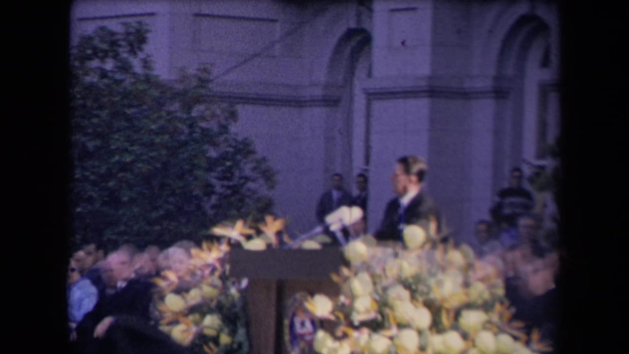 Ronald Reagan stands at a flower-covered podium before a seated outdoor audience.
