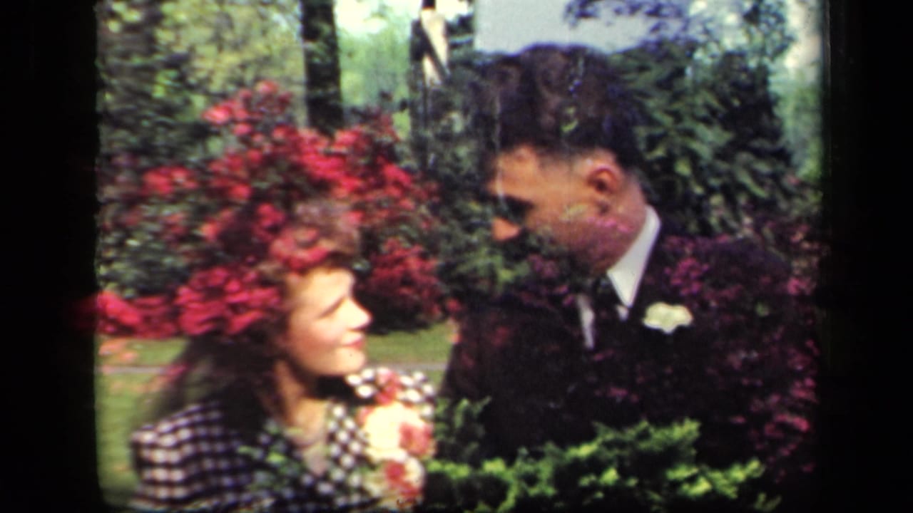 The couple pauses in the garden, looking toward each other among shrubs and bright red flowers in the 1941 New York clip.