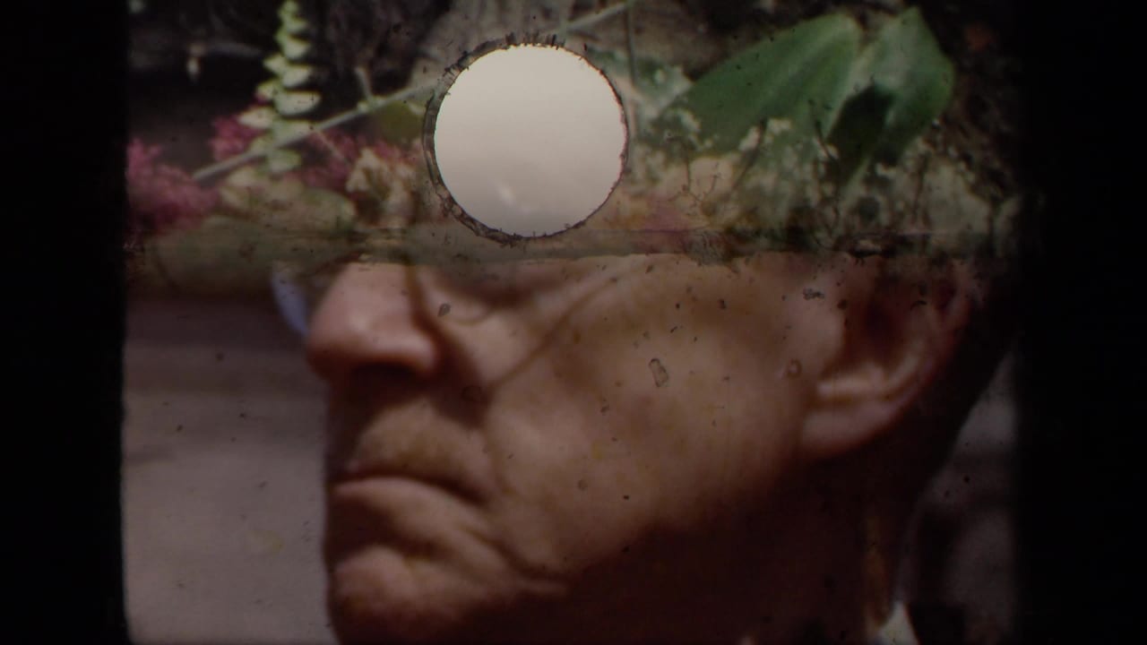 Older man in profile partly obscured by a flower-frame overlay and film damage.