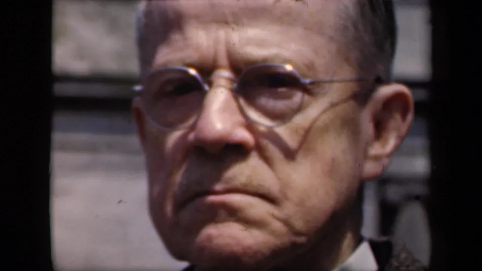 1941 New York 8mm close-up of the older man in round glasses, with soft focus, facial shadow, and blurred exterior background.