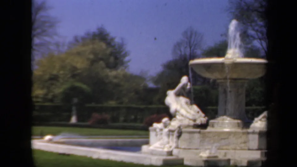 A slightly shifted 1941 8mm view shows the fountain partly centered, with sculpted figures, lawn, railing, trees, and soft color-film grain.