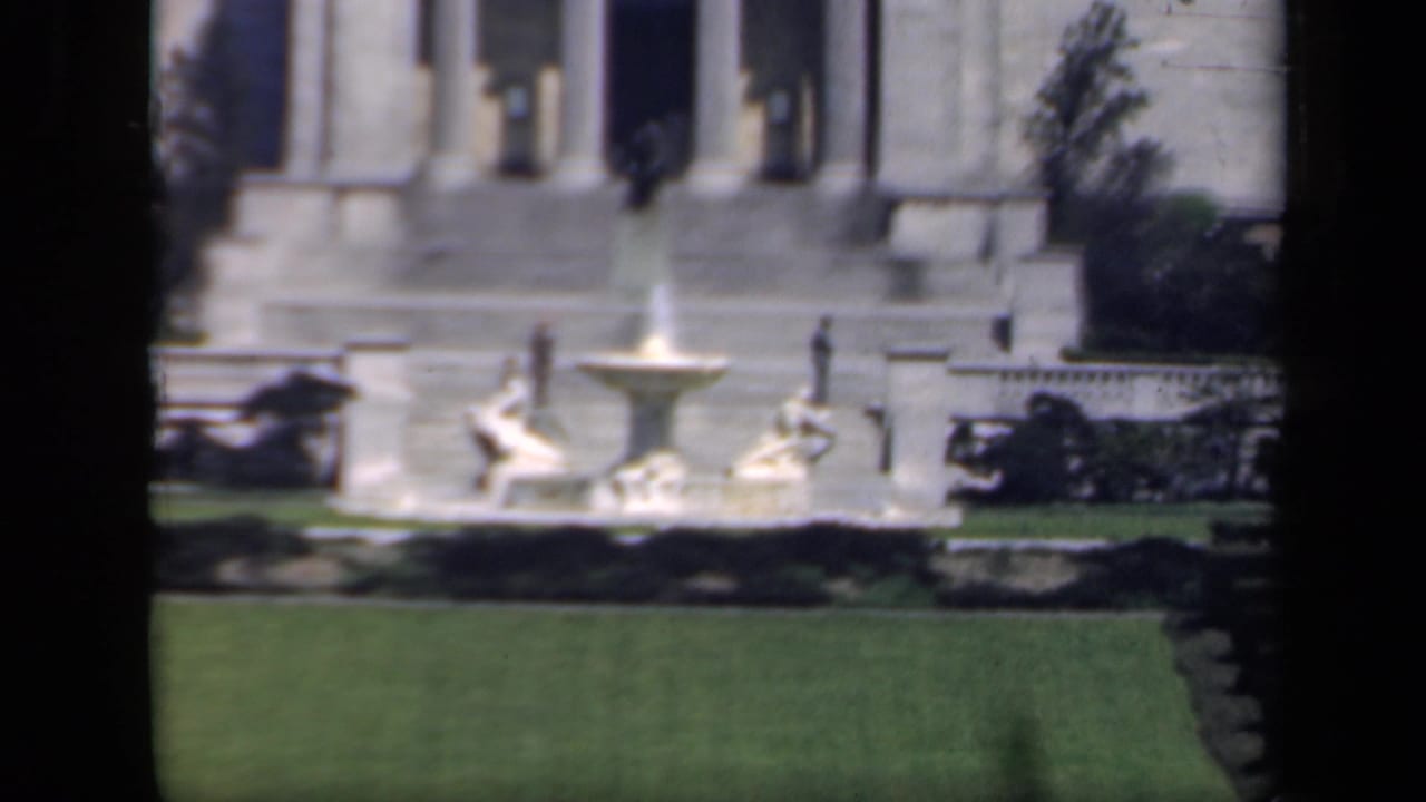 1941 New York home-movie frame showing a lawn fountain, sculptural figures, broad steps, and a columned stone facade.