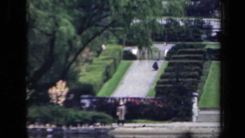 1941 New York 8mm frame of a formal garden path with sculpted hedges, steps, trees, and two distant visitors.
