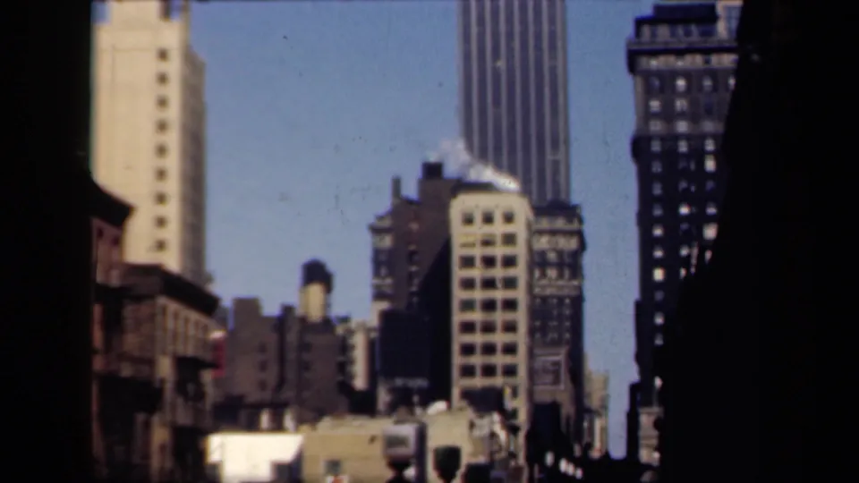 1941 New York street view framed by dark edges, with towers, rooftop equipment, traffic signals, and lower buildings.