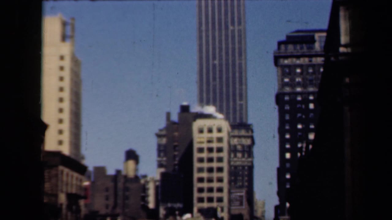 1941 New York home-movie frame showing a tall ribbed skyscraper and nearby high-rises framed by dark vertical edges.
