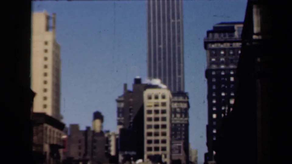 1941 New York home-movie frame showing a tall ribbed skyscraper and nearby high-rises framed by dark vertical edges.