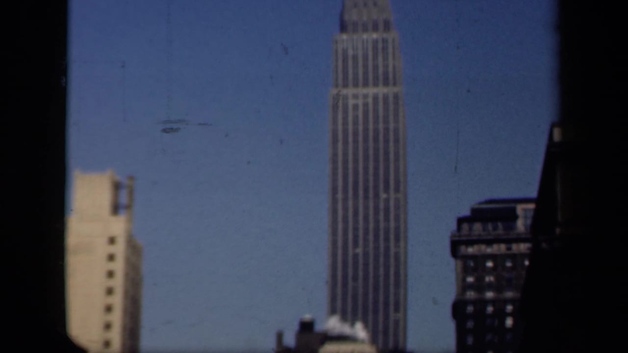 1941 New York 8mm frame showing the Empire State Building rising behind nearby rooftops, viewed through dark window edges.