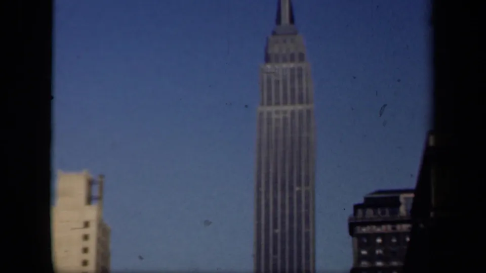 1941 New York home-movie frame with the Empire State Building and adjacent Midtown buildings under a clear blue sky.