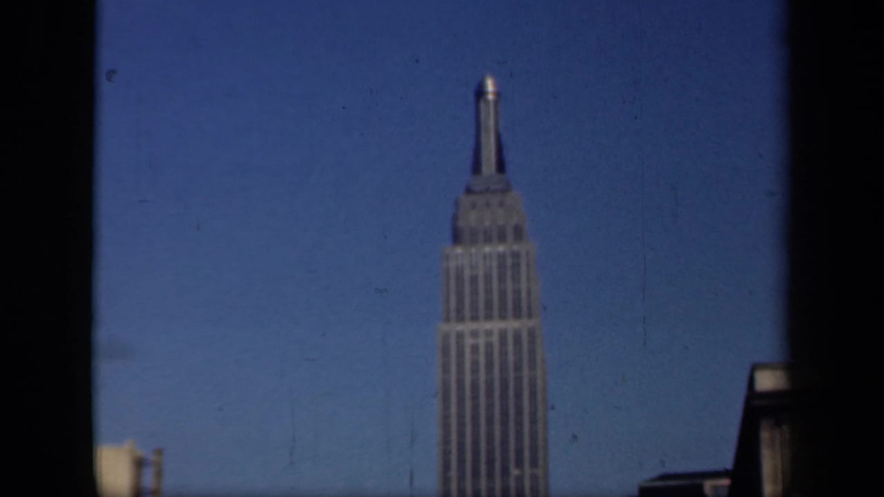 1941 New York home-movie frame showing the Empire State Building rising behind a dark window edge and blue sky.
