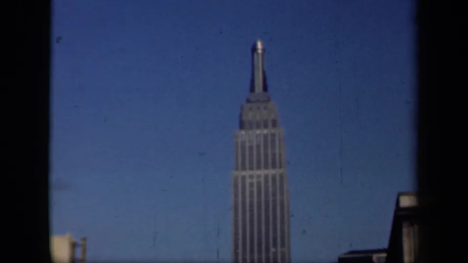 1941 New York home-movie frame showing the Empire State Building rising behind a dark window edge and blue sky.