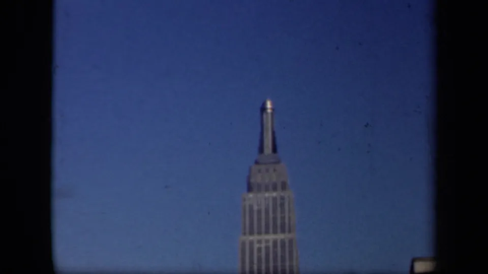 1941 New York home-movie view holding on the Empire State Building with surrounding frame shadows and blue sky.