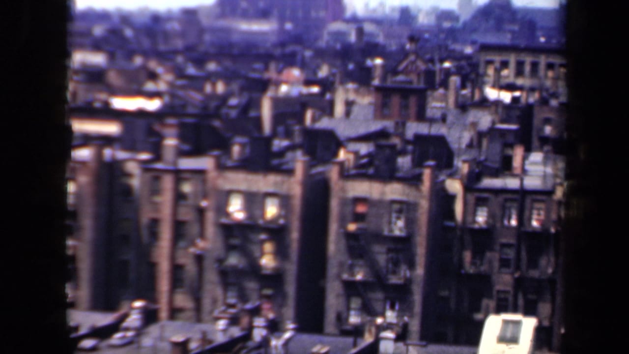 Window-framed view of dense brick apartment buildings and rooftops.
