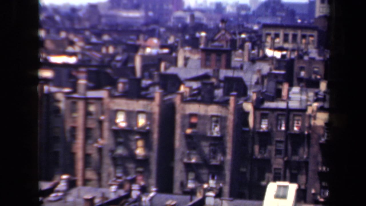 Brick apartment facades and rooftops divided by a dark vertical window frame.