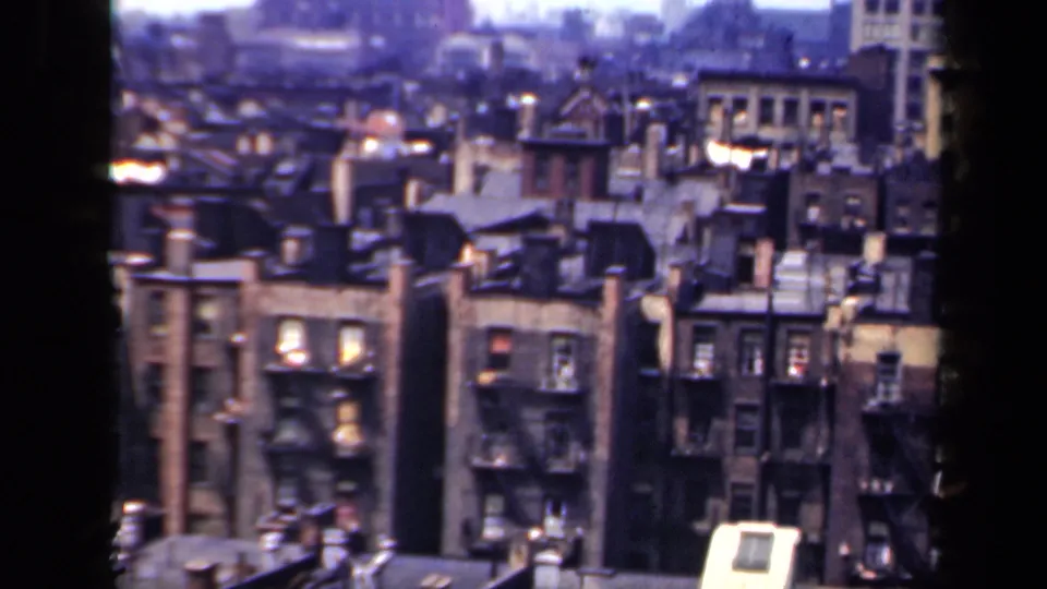 1941 New York home-movie frame showing a dense residential block with fire escapes, rooftops and softened distant buildings.