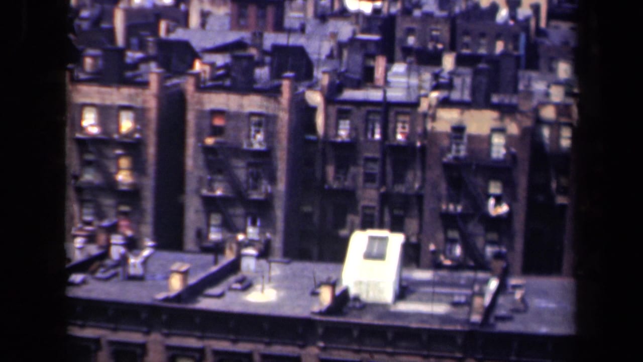 1941 New York overhead view of brick apartment buildings, fire escapes, flat roofs, vents and lit windows.