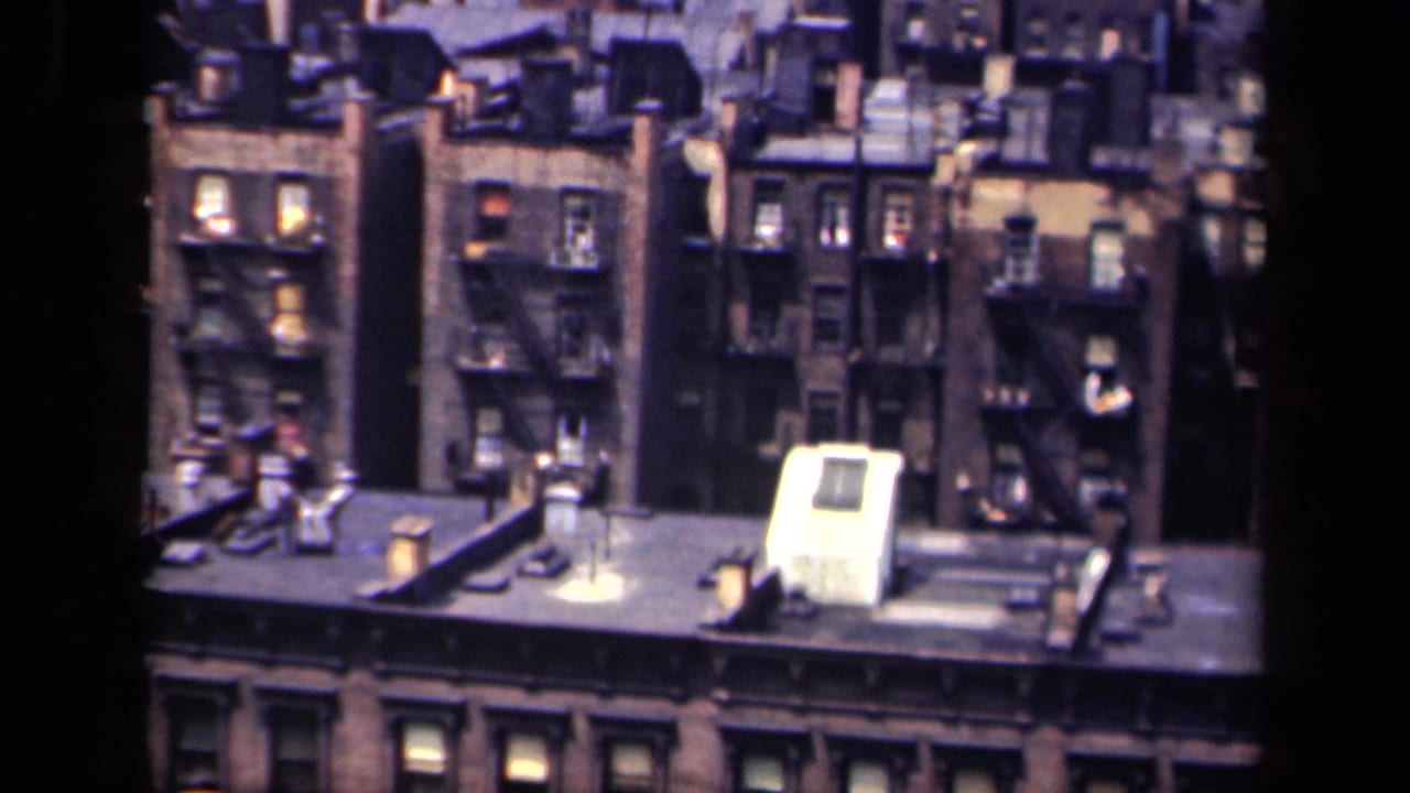 High-angle 1941 New York city view showing brick facades, fire escapes, rooftop vents and illuminated windows.
